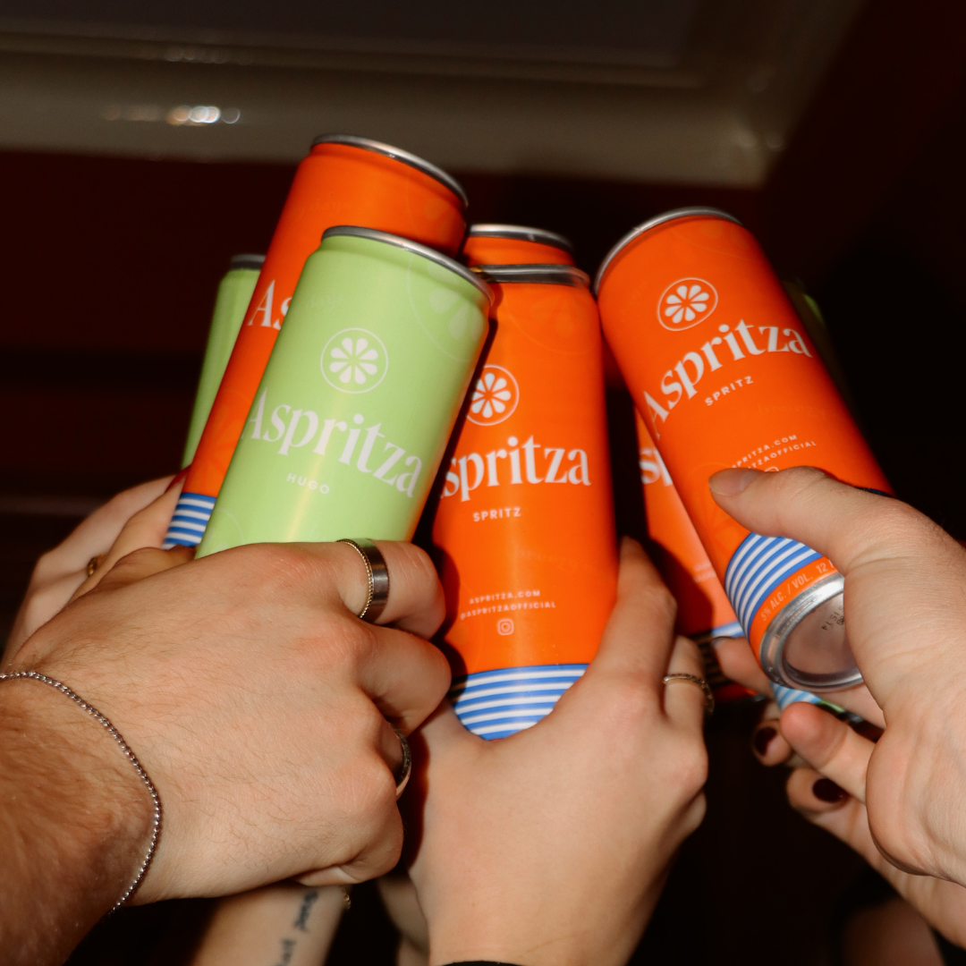 Hands holding Aspritza spritz cans in a close-up shot.