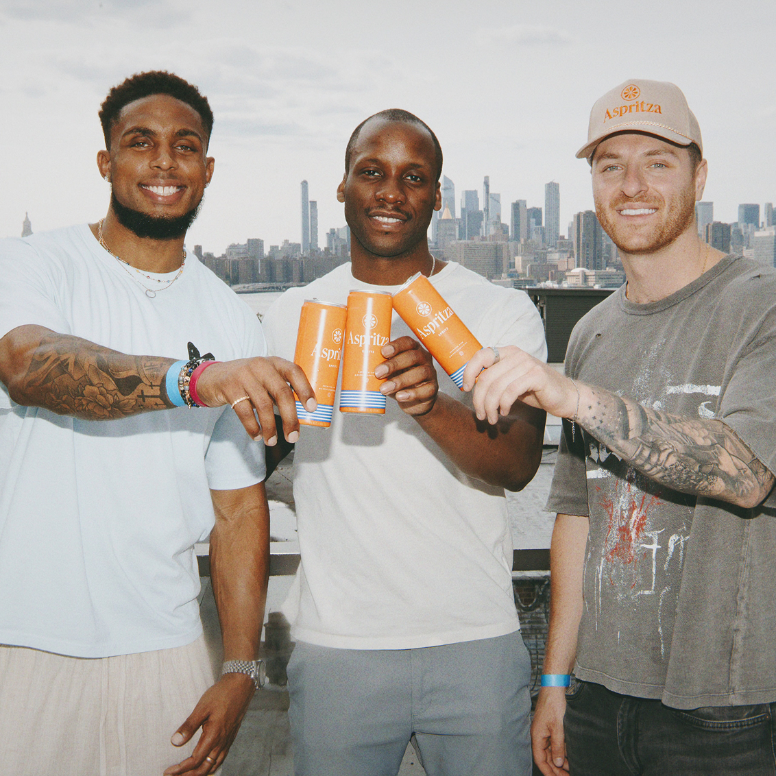 Three men holding orange cups with a cityscape in the background
