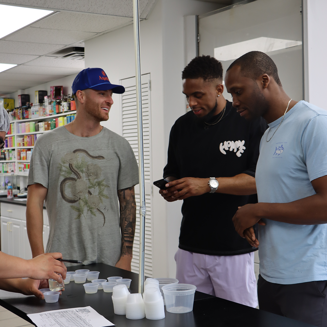 Three men standing around a table with containers and a phone, in a store setting.