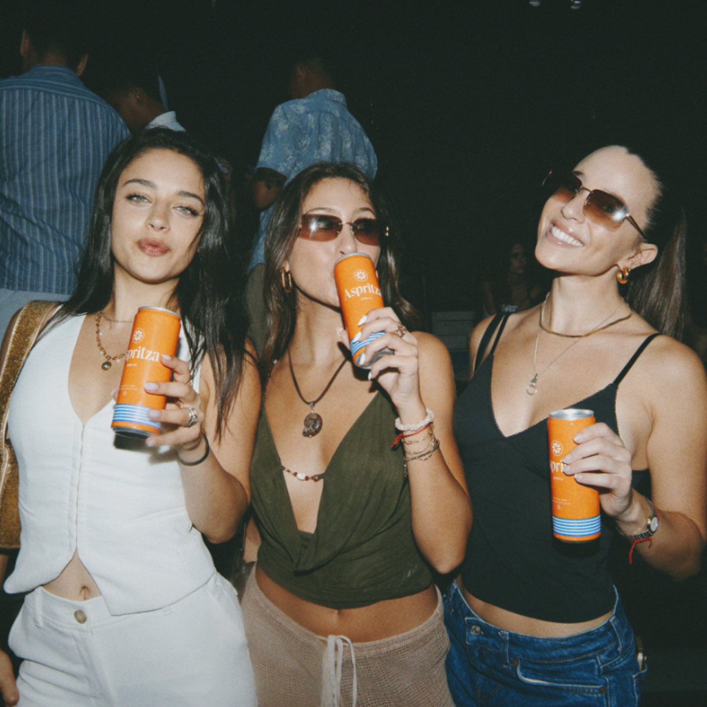 Three women holding orange drinks at a social gathering.