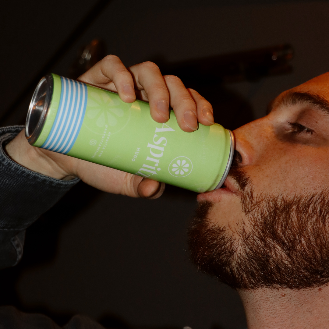 Person drinking from a green can with a brand logo on a dark background