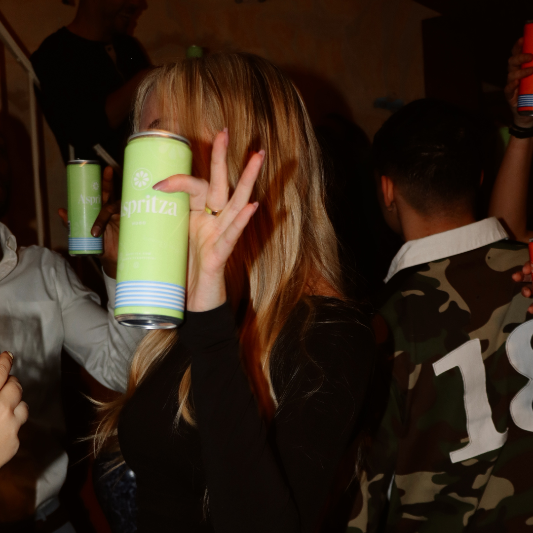 Person holding a green can in a social setting with other people.